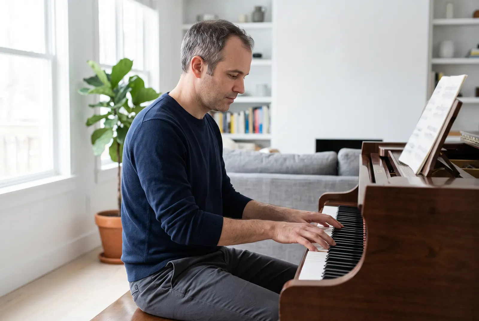 Mann Anfang 40 sitzt an einem Klavier in einem hellen Wohnzimmer und spielt ruhig und konzentriert.